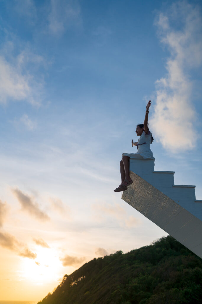 Asian woman raise arms up sit on top of wooden staircase with su mujer asiatica levanta los brazos y se sienta en la parte superior de la escalera de madera con el cielo del atardecer en el fondo la victoria el concepto de exito